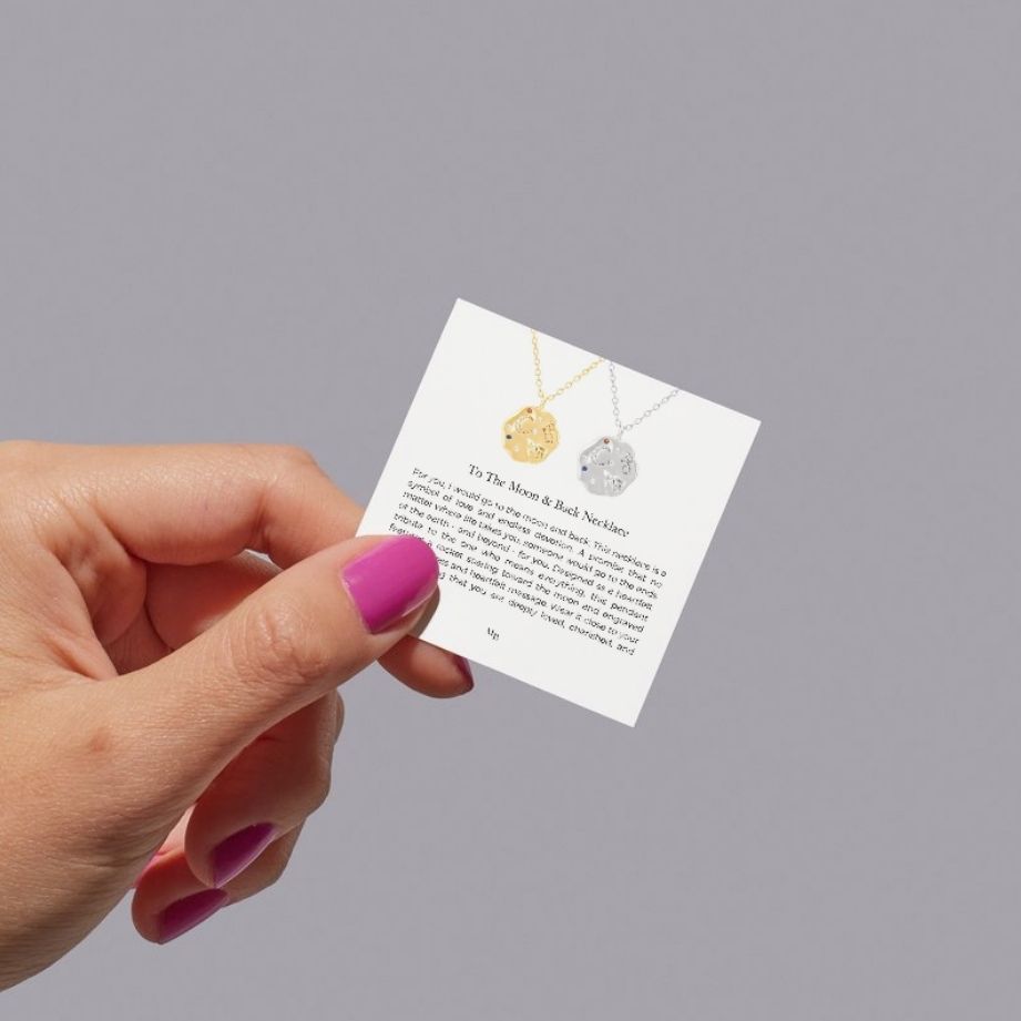 Hand holding a card with two necklaces on it against a gray background